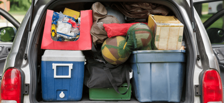 A silver car packed with camping gear, including a tent, sleeping bags, coolers, chairs, and other outdoor equipment. The car is parked in a grassy area, suggesting the camping trip is about to begin.